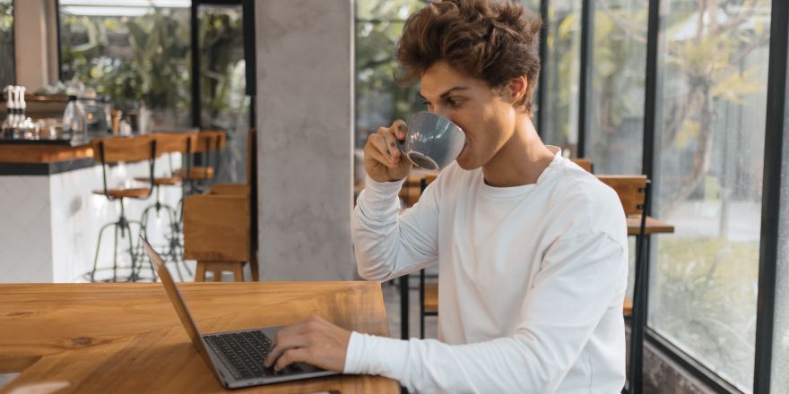 Jongen achter de laptop drinkt een kop koffie