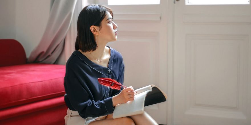 Vrouw in een kamer aan het schrijven met een veer in een schriftje